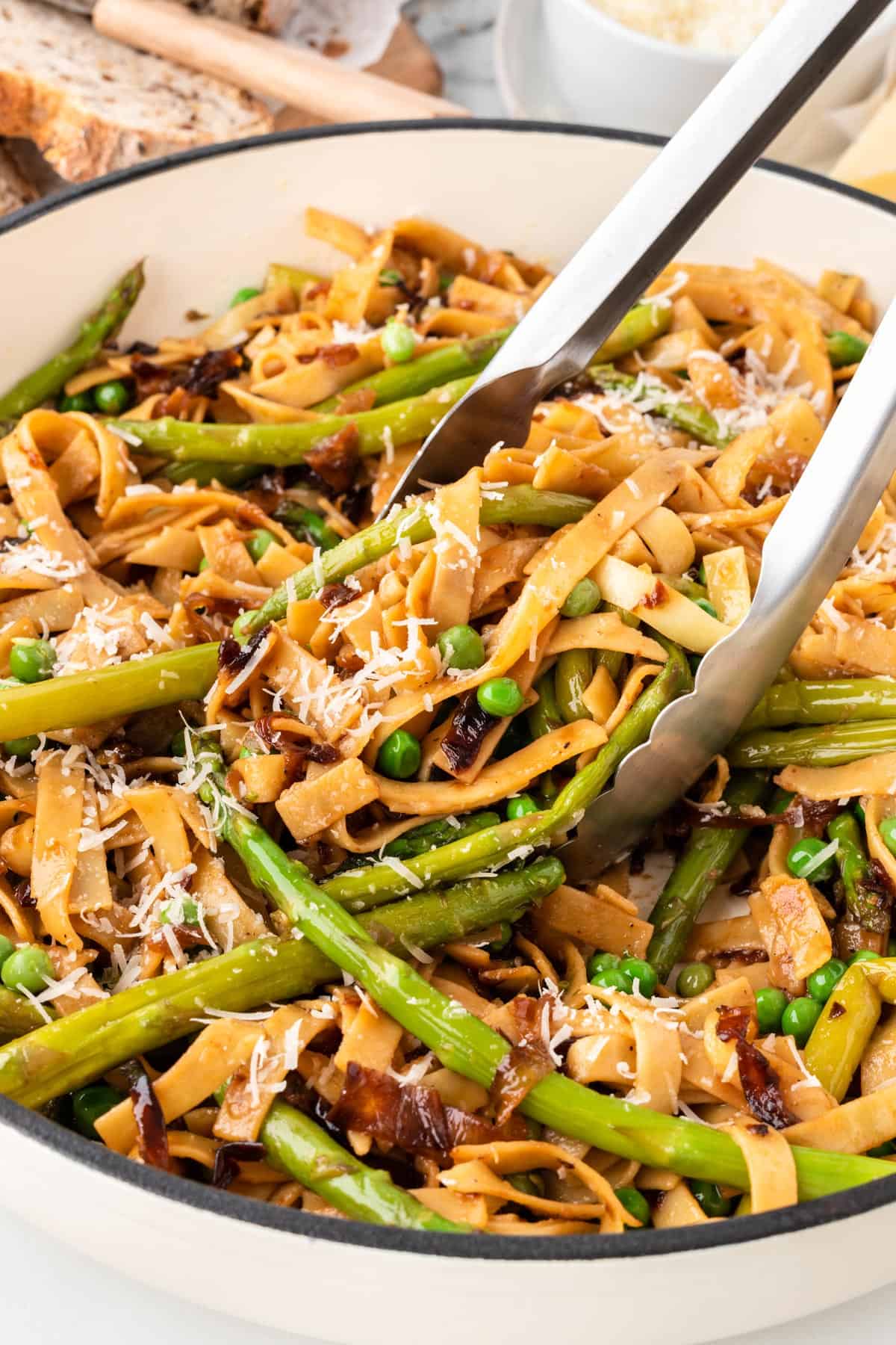 A photo of tongs scooping up asparagus and pea pasta.