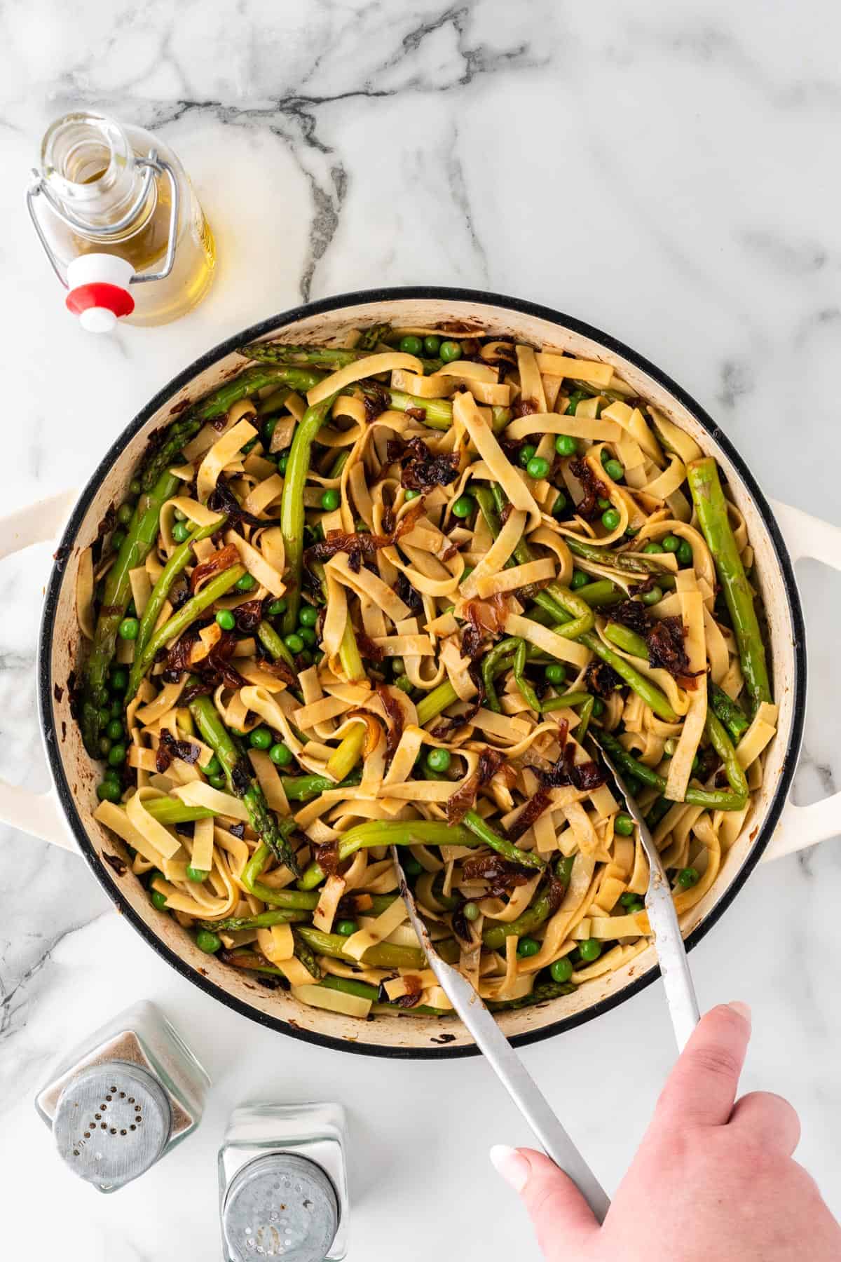 A photo of tossing spring vegetable pasta with tongs.