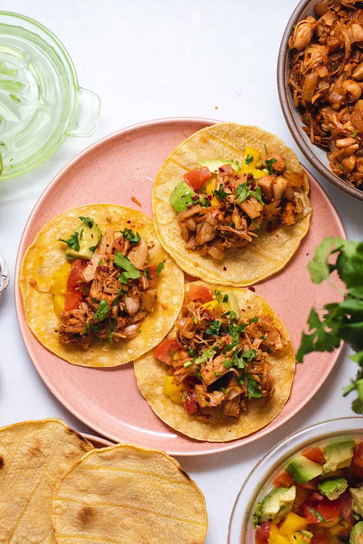 A photo of three small bbq jackfruit tacos on a pink plate.