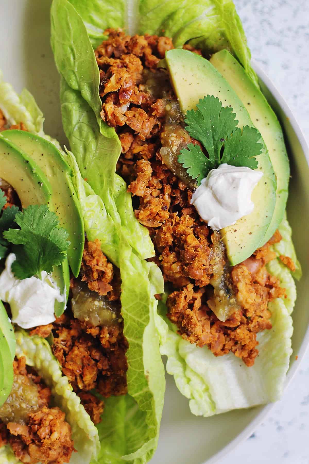 A close up photo of a taco lettuce boat with meatless taco meat substitute, sour cream, and fresh cilantro.