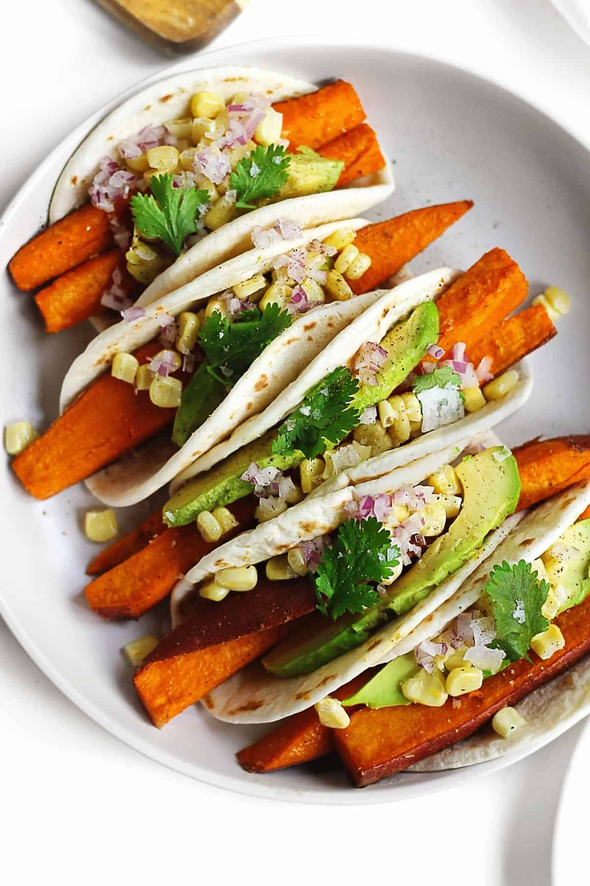 A photo of five small sweet potato tacos on a white plate.