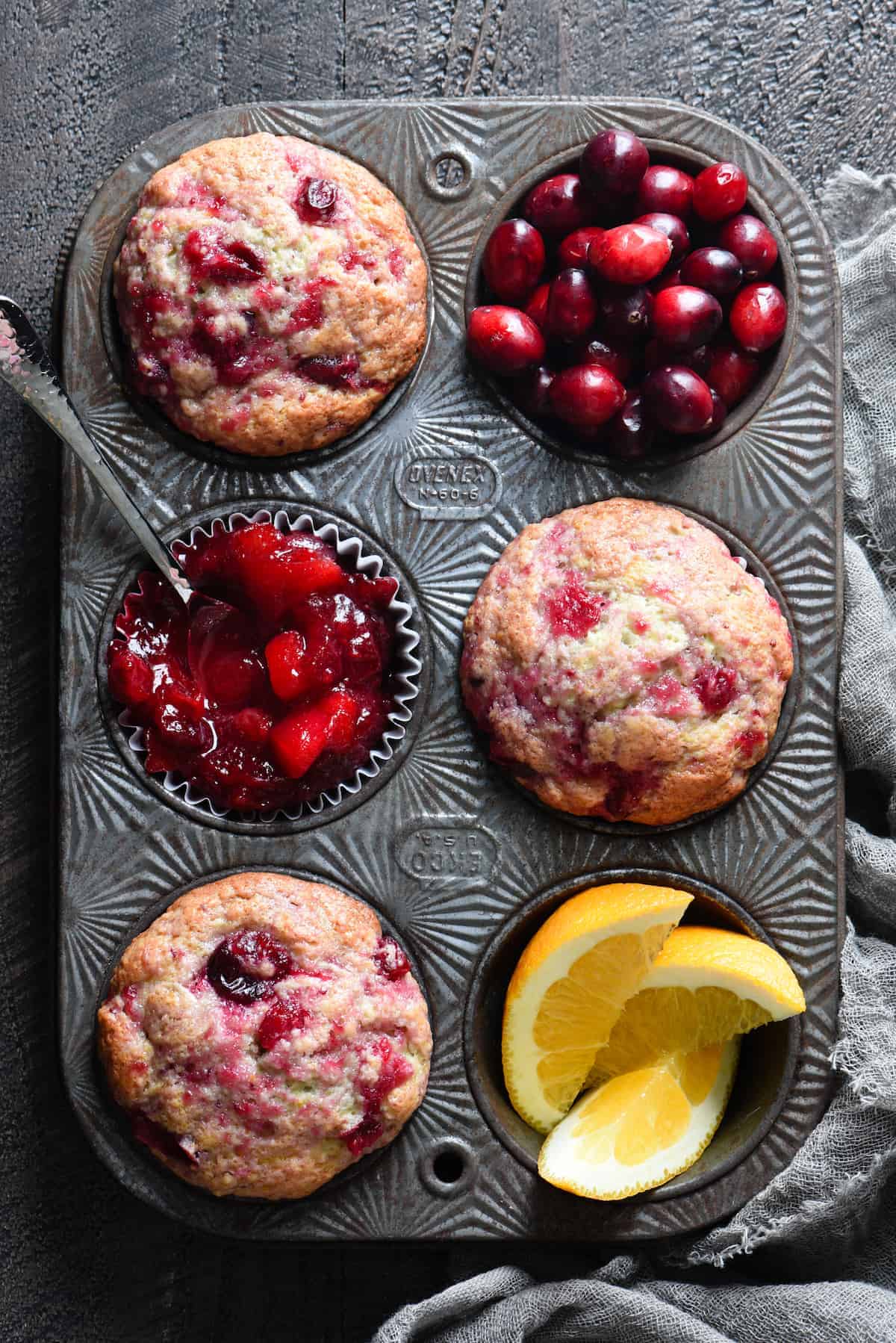 A photo of a muffin tin with cranberry sauce muffins and fresh cranberries in it.