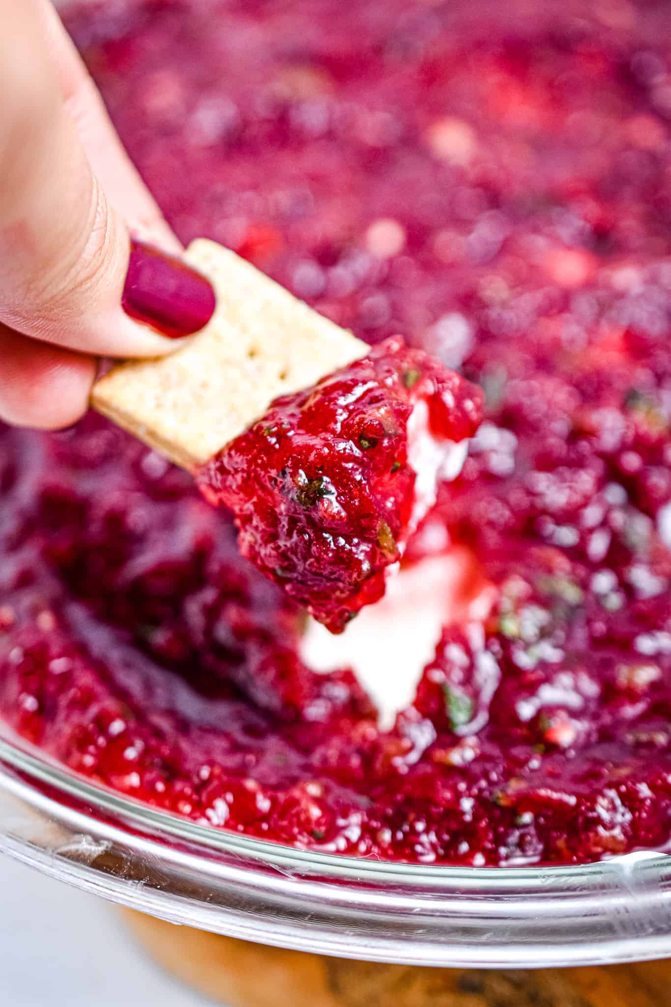 A photo of a cracker dipped in cranberry jalapeno dip.