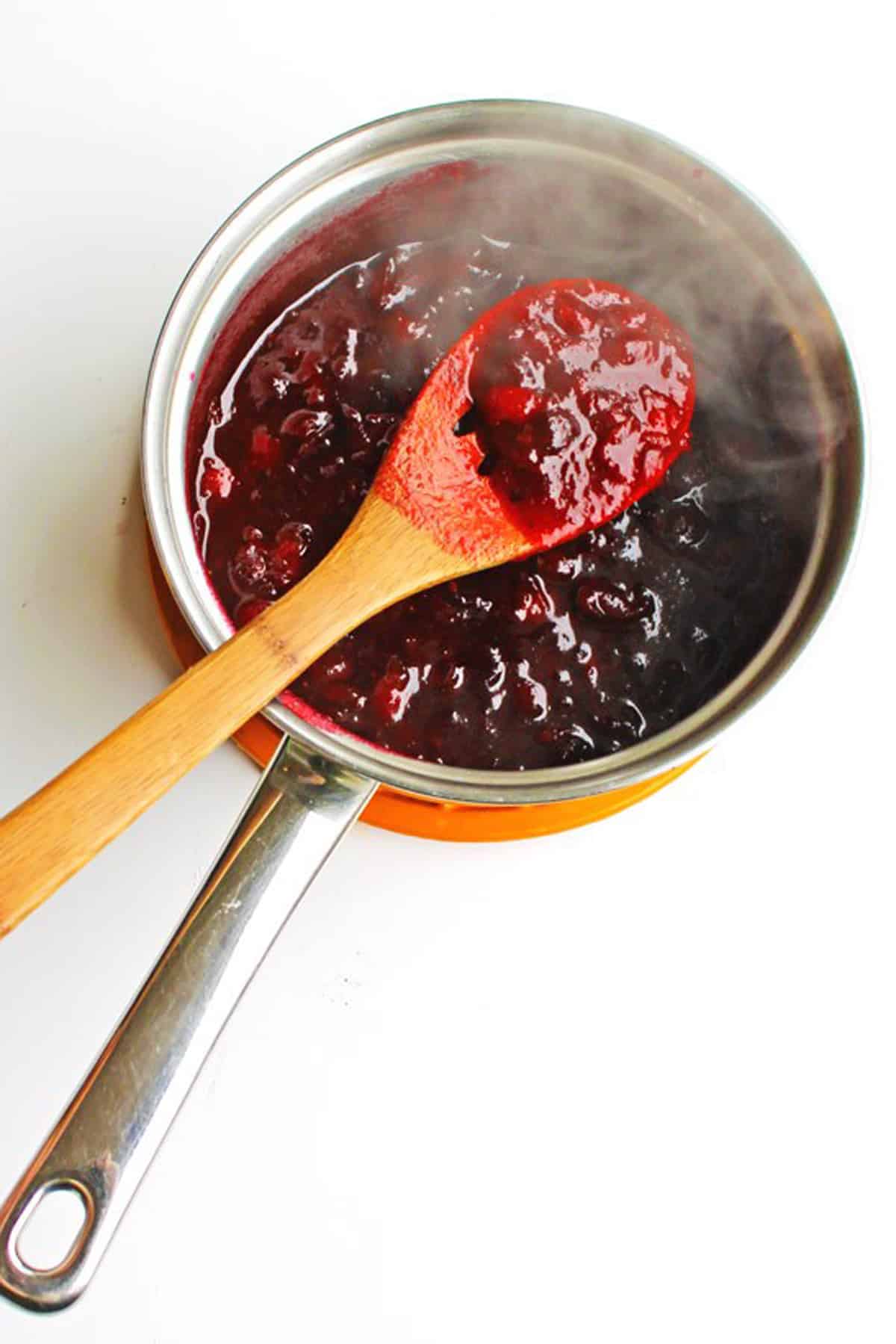 A photo of a wooden spoon in a pan of cooked cranberry sauce.