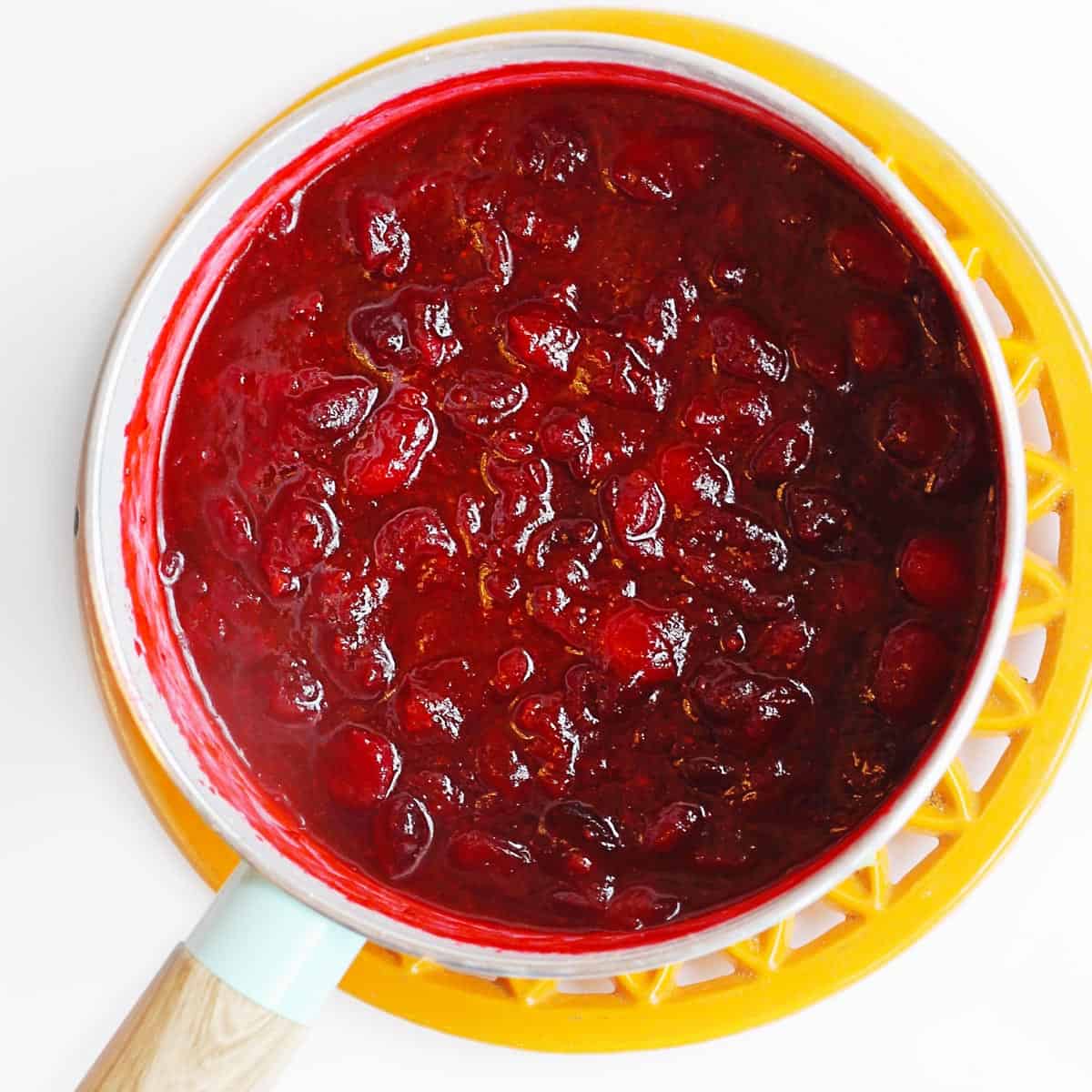 A square photo of whole berry cranberry sauce in a sauce pan.