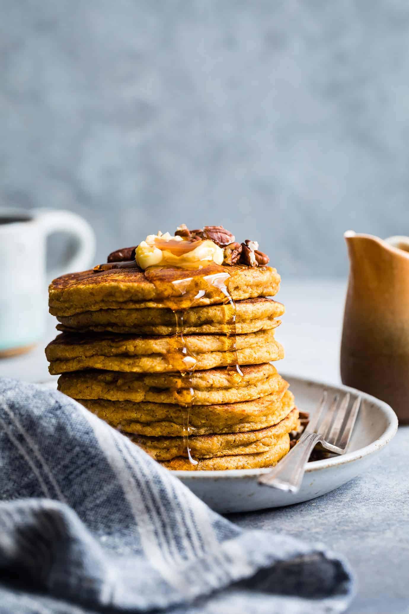 A photo of a stack of pumpkin pancakes with butter, maple syrup, and pecans on top.