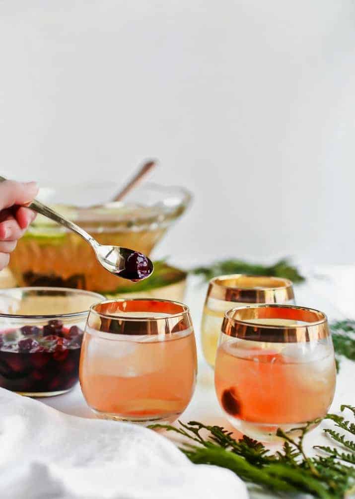 A photo of glasses of holiday whiskey punch with cherries.