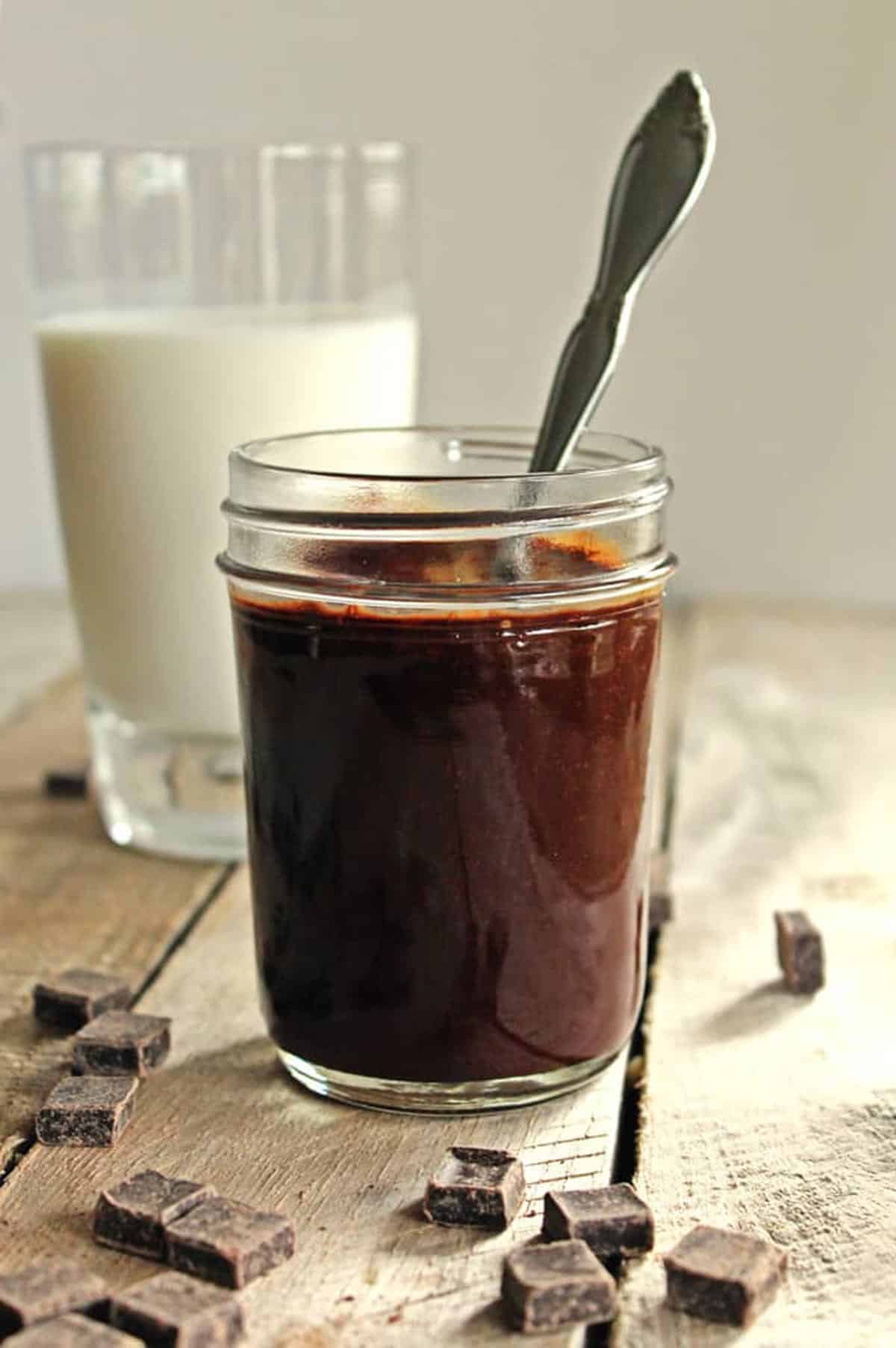 A photo of peanut butter chocolate sauce in a glass jar with a spoon.